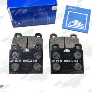 four black square metal brake pads beneath square blue paper on white background