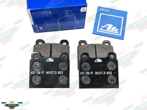 four black square metal brake pads beneath square blue paper on white background